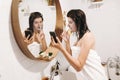 Daily morning routine. Young happy woman in white towel brushing teeth and looking at phone screen in stylish bathroom at round Royalty Free Stock Photo