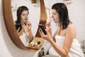 Daily morning routine. Young happy woman in white towel brushing teeth and looking at phone screen in stylish bathroom at round Royalty Free Stock Photo