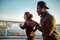 Morning run. Side view of happy sporty African couple in headphones jogging together on the bridge in the early morning Royalty Free Stock Photo