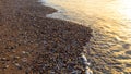 Morning sand - pebble beach illuminated by the first rays of the sun and gentle waves of the sea Royalty Free Stock Photo