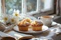 Morning scene by the window of a pair of freshly dusted muffins, a cup of tea and a book. Generative AI