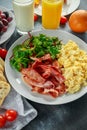 Morning Scrambled egg, bacon breakfast with orange juice, milk, fruit, bread on white plate