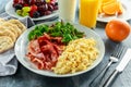 Morning Scrambled egg, bacon breakfast with orange juice, milk, fruit, bread on white plate