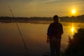 Morning on the lake dawn. A fisherman is standing on the shore next to fishing rods