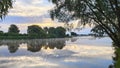 In the morning, the sun rises over the river among the clouds behind the trees. Willows bend their branches over the water. The co Royalty Free Stock Photo