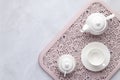 Morning tea party. White ceramic teapot, cup and sugar bowl on a pink openwork tray. Gray marble background. Table setting, flat Royalty Free Stock Photo