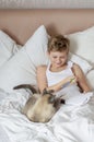 Cute handsome blonde boy lying in white bed. Boy smiling and playing with cat. Relax time Royalty Free Stock Photo