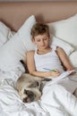 Cute handsome blonde boy lying in white bed. Boy smiling and playing with cat. Relax time Royalty Free Stock Photo