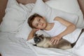 Cute handsome blonde boy lying in white bed and playing with cat. Relax time Royalty Free Stock Photo