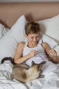 Cute handsome blonde boy lying in white bed. Boy smiling and playing with cat. Relax time Royalty Free Stock Photo