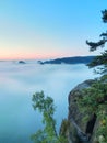 Morning view over rock and fresh green trees to deep valley full of light blue mist. Dreamy spring landscape within daybreak Royalty Free Stock Photo