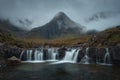 Morning view of a river with a waterfall and a cloud-shrouded mountain peak