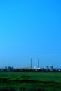 Morning view of a verdant field and pipes of a thermal power plant on the horizon.