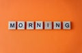 Morning word. The phrase is laid out in wooden letters top view. Orange flat lay background.