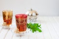 Moroccan tea with mint and sugar in a glass on a white table with a kettle