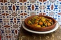 Moroccan vegetable tajine on wooden table, with traditional arabic tiles in the background