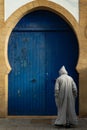 Morocco. Essaouira. A man dressed in a djellaba in front of a blue door