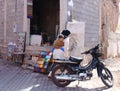 Moroccan woman carrying her child, passing by a motorcycle parked in a street of old city