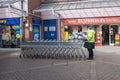 Morrison supermarket worker standing with shopping trolleys in front of Ryman store.