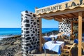 MORRO JABLE, FUERTEVENTURA - FEB 7, 2014: tables and chairs of a restaurant on coast of Morro Jable town. Building is made of lava Royalty Free Stock Photo