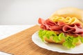Mortadella sandwich, lettuce and cheese on a white plate and a bamboo mat with white background on a table with white towel,