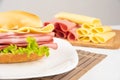 Mortadella sandwich, lettuce and cheese on a white plate on a mat and slices of mortadella and cheese next to it on a cold board Royalty Free Stock Photo