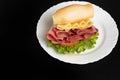 Mortadella sandwich, lettuce and cheese on a white plate on a table with black tablecloth, selective focus