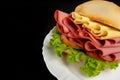 Mortadella sandwich, lettuce and cheese on a white plate on a table with black tablecloth, selective focus