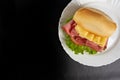 Mortadella sandwich, lettuce and cheese on a white plate on a table with black tablecloth, Top view