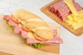 Mortadella sandwich, lettuce, tomato and cheese on a polished board and slices of mortadella and cheese next to it on a cold board