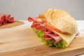 Mortadella sandwich, lettuce, tomato and cheese on a polished board and slices of mortadella and cheese next to it on a cold board