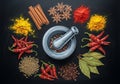 A mortar and pestle are centered on a dark background, surrounded by an array of spices: bright Royalty Free Stock Photo