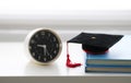 Mortarboard and alarm clock on stack of books, in white