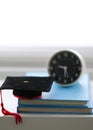 Mortarboard and alarm clock on stack of books, in white