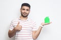 Mortgage is good. Positive attractive young man in t-shirt holding green paper small house and propose you to planning new home to Royalty Free Stock Photo