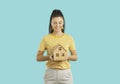 Friendly female realtor holding wooden model house isolated on light blue background. Royalty Free Stock Photo