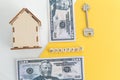 mortgage, loan and home purchase. Model of house, dollar bills, key on white and yellow isolated background. Free space for text, Royalty Free Stock Photo