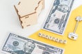 mortgage, loan and home purchase. Model of house, dollar bills, key on white and yellow isolated background. Free space for text, Royalty Free Stock Photo