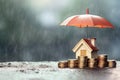 Mortgage protection or renter home insurance. Miniature house model and coins under red umbrella