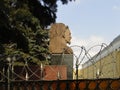 Portrait sculpture of Felix Dzerzhinsky behind a barbed wire fence. Sunny daylight view.