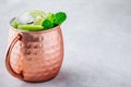 Moscow mule ice cold cocktail in copper cup with lime and and mint on gray stone background