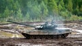 Military tankman runs to tank standing in mud on background of forest.