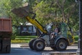 A miniature bulldozer loads gravel into the back of a truck parked on the street