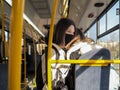 Two cheerful girls in protective masks in a city bus laugh and hug