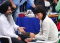 An elderly bearded Indian in a black turban gives a woman an acupressure of the hand