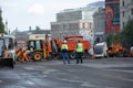 Two workers in riot gear stand in front of heavy construction equipment and cargo vehicles.