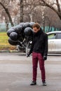 Birthday is a sad holiday concept. A young blonde man wearing black scarf and coat guy holding black balloons and smoking. Royalty Free Stock Photo