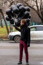 Birthday is a sad holiday concept. A young blonde man wearing black scarf and coat guy holding black balloons and smoking. Royalty Free Stock Photo