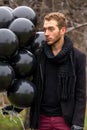 Birthday is a sad holiday concept. A young blonde man wearing black scarf and coat holding black balloons going down street Royalty Free Stock Photo