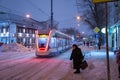 Moscow, Russia - December 7, 2022: An elderly woman crosses the road. Tram rides through the winter snowy city